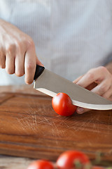Image showing male hand cutting tomato on board with knife