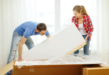 Image showing smiling couple opening big cardboard box with sofa