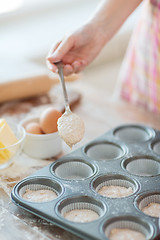 Image showing close up of hand filling muffins molds with dough