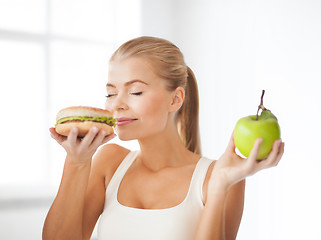Image showing smiling woman smelling hamburger and holding apple