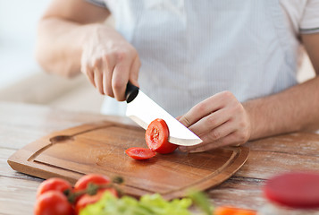 Image showing male hand cutting tomato on board with knife