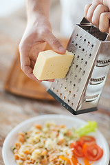 Image showing close up of male hands grating cheese over pasta