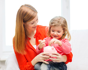 Image showing happy mother and daughter with small piggy bank