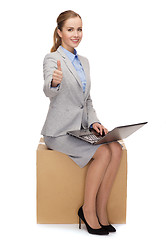 Image showing smiling woman sitting on cardboard box with laptop