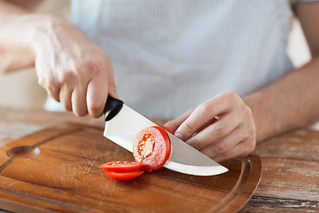 Image showing male hand cutting tomato on board with knife