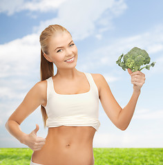 Image showing woman pointing at her abs and holding broccoli