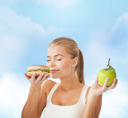 Image showing happy woman smelling hamburger and holding apple