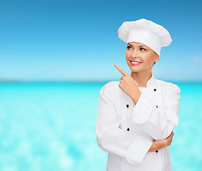 Image showing smiling female chef pointing finger to sonething