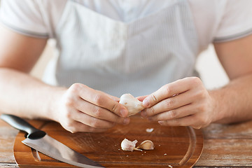 Image showing male hands taking off peel of garlic on board