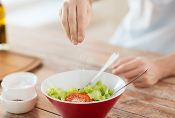 Image showing close up of male hands flavouring salad in a bowl