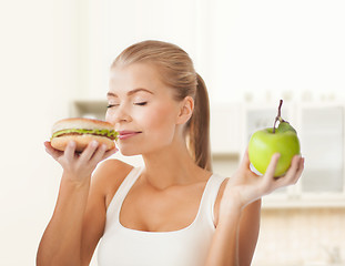 Image showing happy woman smelling hamburger and holding apple