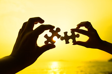 Image showing Two hands trying to connect puzzle pieces with sunset background