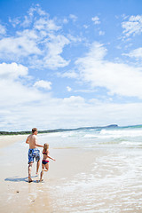 Image showing Father and young daughter running along beach