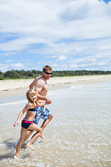 Image showing Happy father and daughter running along beach in shallow water