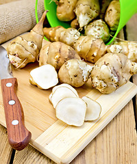 Image showing Jerusalem artichokes cut with knife and bucket on board