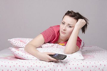 Image showing The tired girl lying in bed and watching TV