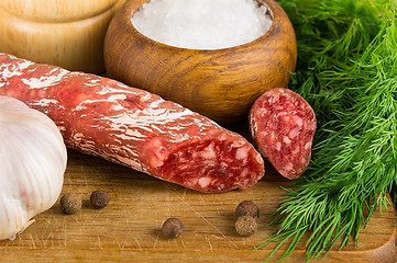 Image showing sliced salame on cutting board, with dill, pepper, salt