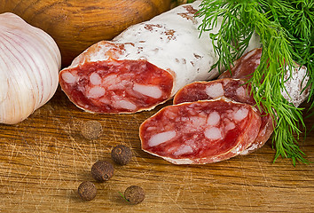 Image showing sliced salame on cutting board, with dill and pepper