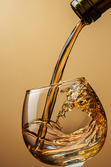 Image showing Cognac pouring from bottle into glass with splash on brown backg