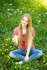 Image showing Smiling female sitting on the field of dandelions