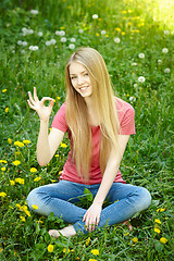 Image showing Smiling female sitting on the field of dandelions