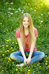 Image showing Smiling female sitting on the field of dandelions