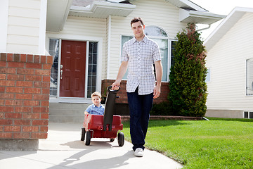 Image showing Father Pulling Son Sitting Inside Wagon