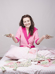 Image showing Joyful girl sitting on bed with a bundle of money