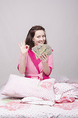 Image showing Young girl sitting in bed with a bundle of money