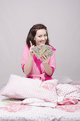 Image showing Happy girl sitting in bed with a bundle of money