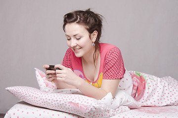 Image showing Happy girl writes SMS in bed