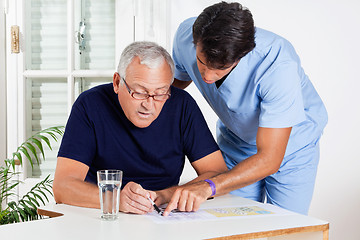 Image showing Male Nurse Helping Senior Man In Solving Puzzle