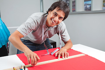 Image showing Happy Dressmaker Measuring Red Fabric