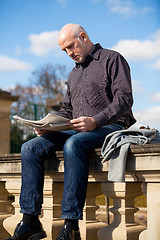 Image showing Man sitting reading a newspaper on a stone wall