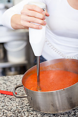 Image showing Woman chef whisking boiled tomato sauce in a pot