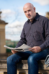 Image showing Man sitting reading a newspaper on a stone wall