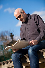 Image showing Man sitting reading a newspaper on a stone wall