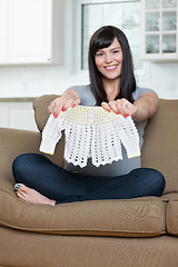 Image showing Pregnant Woman Holding Baby Clothing On Sofa