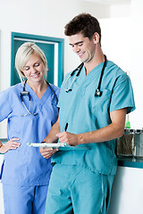 Image showing Male Doctor Writing On Clipboard With Colleague At Clinic