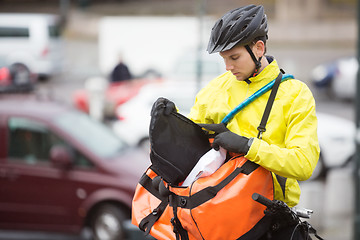 Image showing Young Male Cyclist Putting Package In Courier Bag