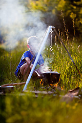 Image showing Little boy cooks on a fire in wood