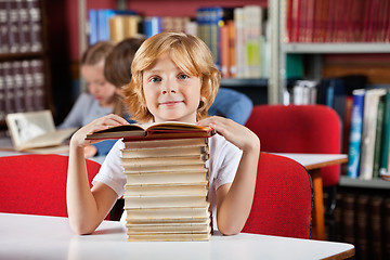 Image showing Schoolboy Sitting With Stack Of Books In Library