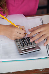 Image showing Teenage Schoolgirl Using Calculator While Writing At Desk