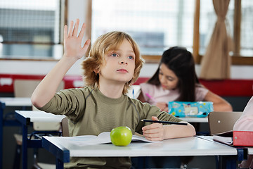 Image showing Schoolboy Looking Away While Raising Hand At Desk