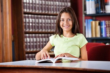 Image showing Schoolgirl With Book Sitting At Table In Library