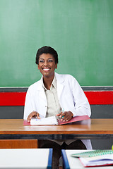 Image showing Happy Teacher Looking Away While Sitting With Binder At Desk