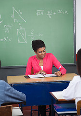 Image showing Teacher Writing In Binder At Desk With Students In Foreground