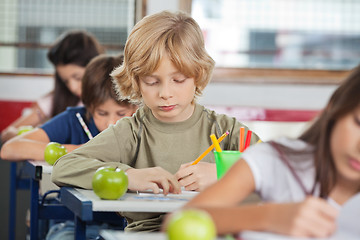 Image showing Schoolboy Writing While Sitting At Desk