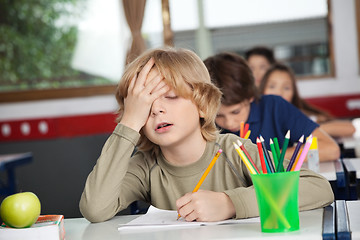 Image showing Tired Schoolboy Sitting At Desk In Classroom