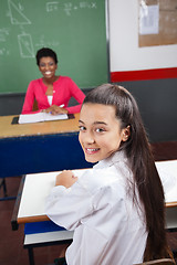 Image showing Schoolgirl Sitting At Desk With Teacher Smiling In Background